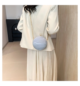 Fashionable round evening bag with crumpled paper texture and golden chain on a model