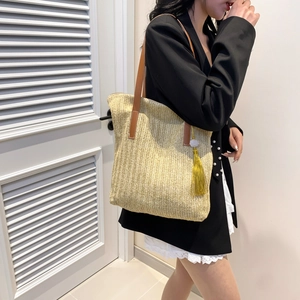 Fashionable woven straw tote bag with brown leather straps and yellow tassel accessory