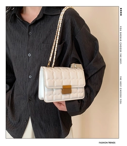 Detail view of white quilted crossbody bag with gold chain strap worn by a fashion model