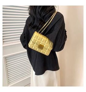 Close-up of golden quilted chain bag worn by model, showing detailed texture and metallic lock