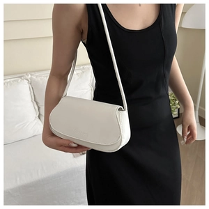 Sac à bandoulière blanc en similicuir avec embossage porté par un mannequin dans un décor doux