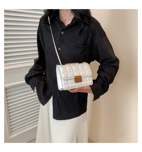 Detail of white quilted handbag with a golden chain strap and metallic rectangular lock