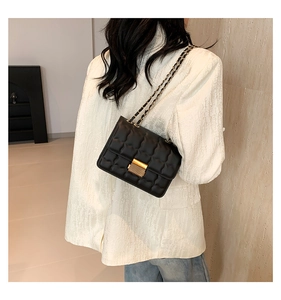 Sac bandoulière matelassé noir avec fermoir doré et chaîne porté sur un tailleur blanc