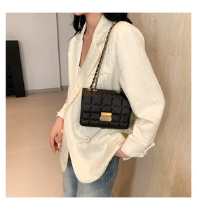 Détail du sac matelassé noir avec fermoir doré et bandoulière chaîne sur un blazer
