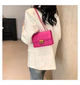 Detailed view of magenta quilted crossbody bag with gold lock and chain strap on model