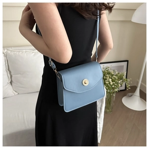 Détail du sac bandoulière en cuir bleu ciel montrant la boucle dorée et la bandoulière