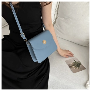 Sac bandoulière en cuir bleu nuage avec boucle dorée porté par un mannequin
