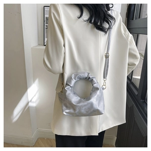 Detail of silver metallic pleated handbag featuring a unique circular handle and gold hardware