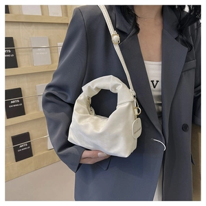 Detail of white ruched dumpling bag featuring circular fashion tag and slim shoulder strap