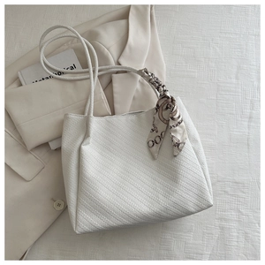 White textured tote bag with silk scarf detail on handle placed near beige blazer