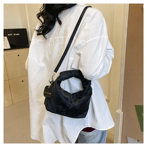 Detail of black pleated crossbody bag with gold chain charm on a model in white shirt
