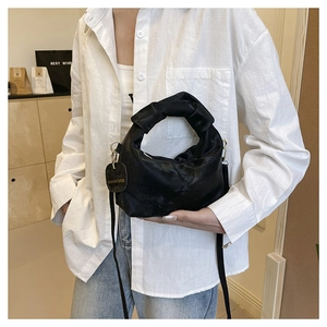 Detail of black pleated cloud bag with knotted handle and elegant metal strap attachment