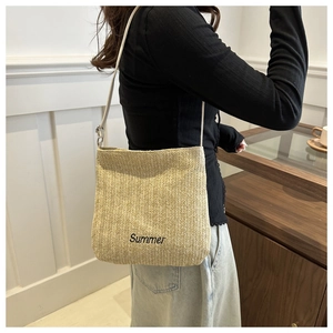 Detail of a beige straw tote bag with black Summer embroidery and white shoulder straps