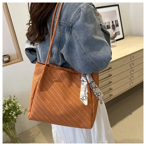 Detail of orange woven tote bag with decorative chain pattern silk scarf on handle