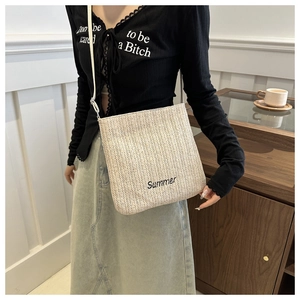 Close-up of beige woven straw tote bag with black Summer embroidery and slim white strap