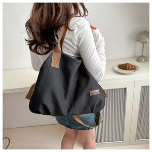 Detail of black canvas tote bag with brown woven straps and leather fashion label