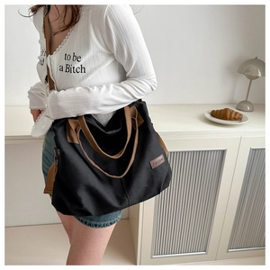 Black canvas tote bag detail with brown leather logo patch and matching handles