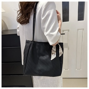 Detail of black tote bag with textured surface and decorative scarf on handle