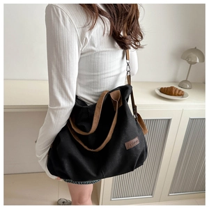 Detail view of large black canvas tote bag with brown straps and fashion leather patch