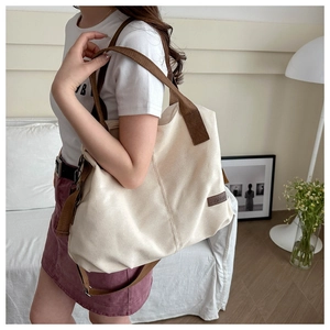 Detail view of large canvas tote bag with brown straps and leather fashion label