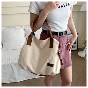 Large beige canvas tote bag with brown straps and fashion label worn by a model