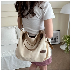 Detail of a large beige canvas tote bag with brown straps worn as a crossbody bag