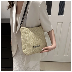Detailed view of beige straw tote bag with black Summer embroidery on model shoulder