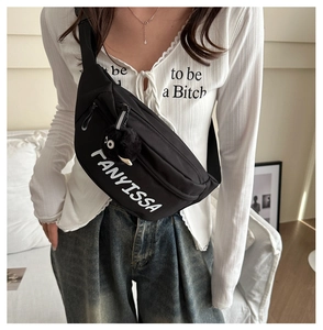 Detail van zwarte nylon crossbodytas met witte tekst en een pluche sprite-hanger