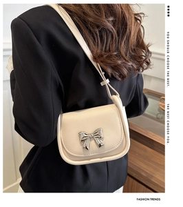 Détail du mini sac selle crème avec nœud en métal argenté et texte tendance sur le côté