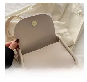 Gros plan du fermoir magnétique doré sur un sac bandoulière de type selle couleur blanc cassé