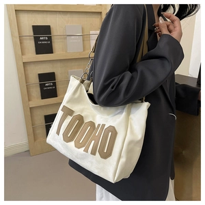 Detail of white tote bag with large brown letter patch and metal chain strap on model