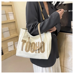 Detail of white leather tote bag with brown TOOHO letter patch and shoulder strap