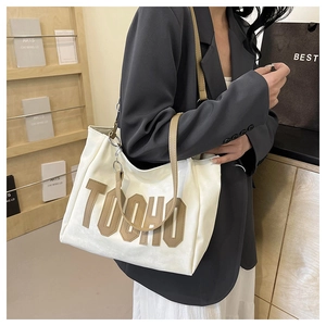 Close-up of cream tote bag with contrast tan TOOHO letter embroidery and slim leather strap
