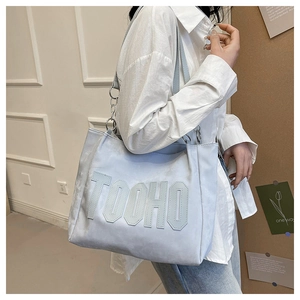 Detail of light blue tote bag with TOOHO lettering and metal chain strap on model