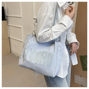 Detail of light blue tote bag featuring TOOHO letter patch and silver chain strap ornament