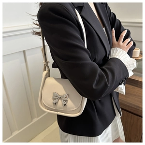 Mini sac selle crème avec nœud argenté porté par un mannequin en tenue chic noir et blanc