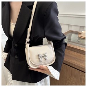Détail du sac besace en cuir blanc crème avec nœud argenté porté par un mannequin