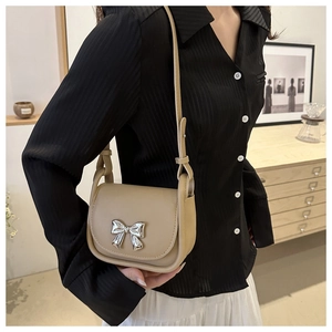 Détail d'un sac bandoulière beige avec un nœud en métal argenté 3D et rabat