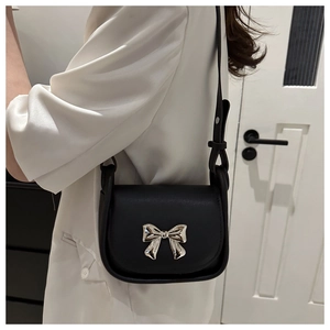 Détail du sac bandoulière en cuir noir avec nœud argenté sur une chemise en satin blanc