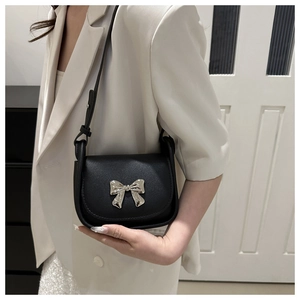 Détail d'un sac bandoulière noir avec nœud en métal argenté sur un mannequin en costume