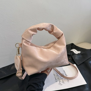 Pale pink pleated dumpling bag with ruffled handle and heart charm on black jacket background