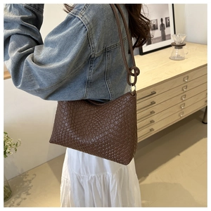 Close-up of the woven leather texture and metal buckle detail on a brown shoulder bag