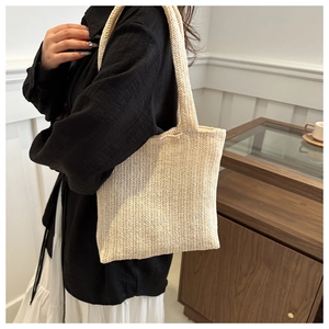 Detail of beige woven tote bag showing herringbone texture and shoulder strap