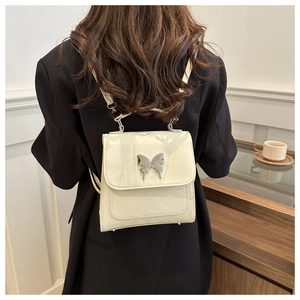 Cream white crossbody bag with butterfly buckle detail worn in a modern cafe setting