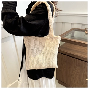 Close-up of beige woven tote bag with herringbone knit texture on a shoulder strap