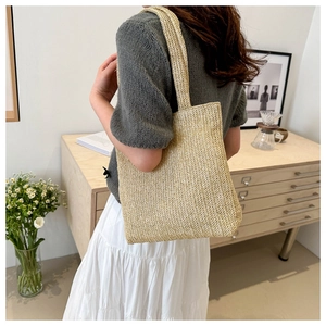 Close-up of woven beige straw tote bag with integrated shoulder strap in a cozy home setting
