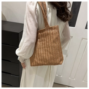 Detail of a brown woven tote bag showing the textured herringbone pattern and long strap