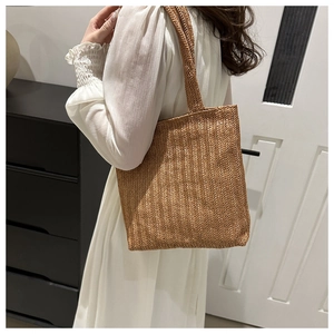 Detailed close-up of brown woven tote bag showing herringbone texture and long handles