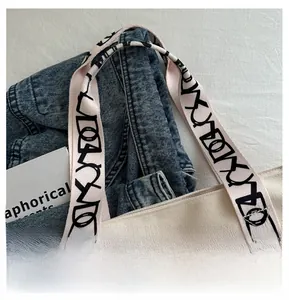 Détail du sac fourre-tout en toile avec sangle imprimée à côté d'une veste en jean