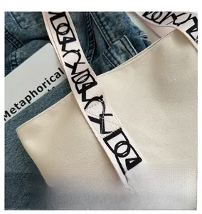 Gros plan du sac cabas en toile crème avec bandoulière brodée et tenue en jean